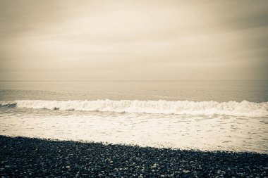 Arka plan, deniz temalı duvar kâğıdı. Sahilde dalgalar. Deniz kıyısı kayalık çakıl taşlarından yapılmıştır. Çoğunlukla bulutlu. Gün, bahar, Georgia.