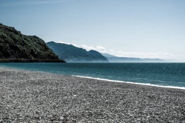 Sahilden dağ manzarası. Çakıl taşından yapılmış deniz kıyısı. Karadeniz 'de dalgalar. Georgia 'da bahar, güneşli bir gün. Hafif rüzgar ve beyaz bulutlar. Dağların bir kısmı yeşillikte, bir kısmı karda.