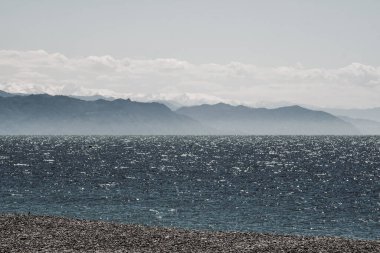 Sahilden dağ manzarası. Çakıl taşından yapılmış deniz kıyısı. Karadeniz 'de dalgalar. Georgia 'da bahar, güneşli bir gün. Hafif rüzgar ve beyaz bulutlar. Dağların bir kısmı yeşillikte, bir kısmı karda.