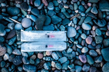 Deniz çakıllarından oluşan arka planda bir çift tek kullanımlık şırınga. Terk edilmiş şırınga. Halka açık yerlerde bağımlılar. Karadeniz kıyısındaki şehir plajı.