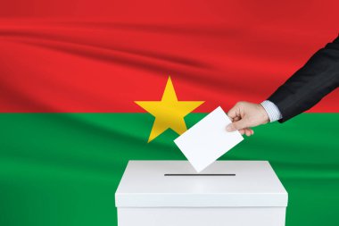 Burkina Faso 'da seçim. Oylarını sandığa koyan adamın eli. Arka planda Burkina Faso bayrağı salladı.