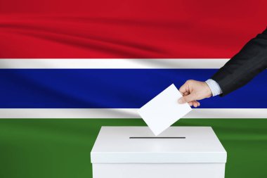 Gambiya 'da seçim. Oylarını sandığa koyan adamın eli. Arka planda dalgalı Gambiya bayrağı.                               
