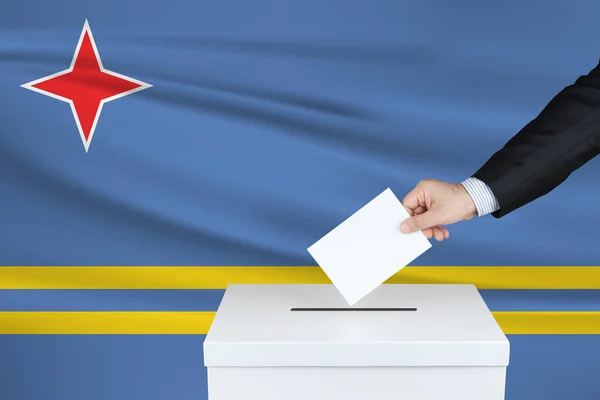 阿鲁巴的选举 把他的选票放进投票箱的人的手 背风飘扬的阿鲁巴国旗 — 图库照片