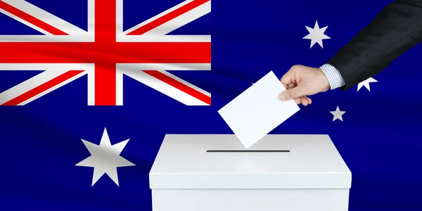 Election in Australia. The hand of man putting his vote in the ballot box. Waved Australia flag on background.