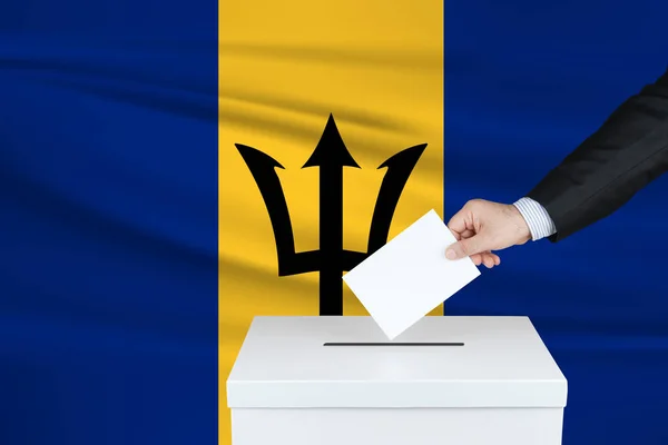Election in Barbados. The hand of man putting his vote in the ballot box.  Waved Barbados flag on background. - Stock Image - Everypixel