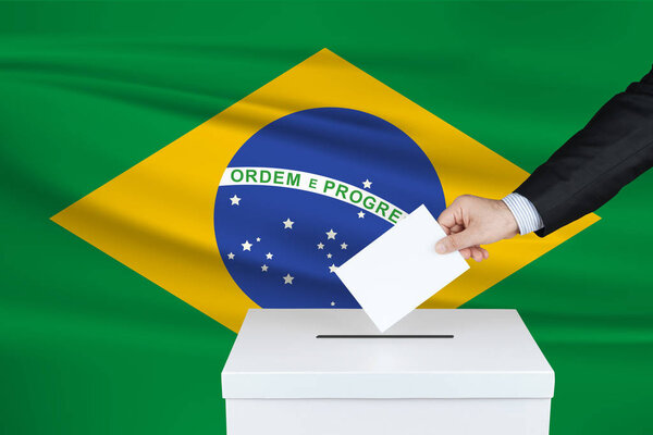 Выборы в Бразилии. Рука человека, положившего свой голос в урну для голосования. Размахивал флагом Бразилии на фоне
.