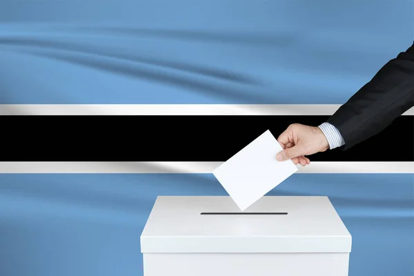 博茨瓦纳的选举 把他的选票放进投票箱的人的手 背景上飘扬的博茨瓦纳国旗 — 图库照片
