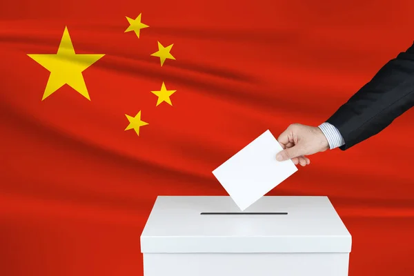 Election in China. The hand of man putting his vote in the ballot box. Waved China flag on background.