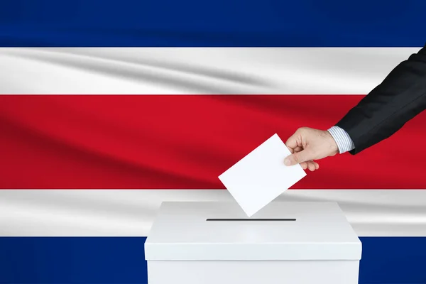哥斯达黎加的选举 把他的选票放进投票箱的人的手 背景上飘扬的哥斯达黎加国旗 — 图库照片