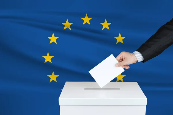 欧洲联盟的选举 把他的选票放进投票箱的人的手 背景下飘扬的欧洲联盟旗帜 — 图库照片