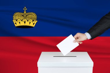 Lihtenştayn 'da seçim. Oylarını sandığa koyan adamın eli. Arka planda Liechtenstein bayrağı sallandı.                               