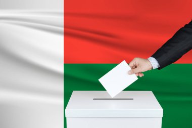 Madagaskar 'da seçim. Oylarını sandığa koyan adamın eli. Arka planda Madagaskar bayrağı salladı.                               
