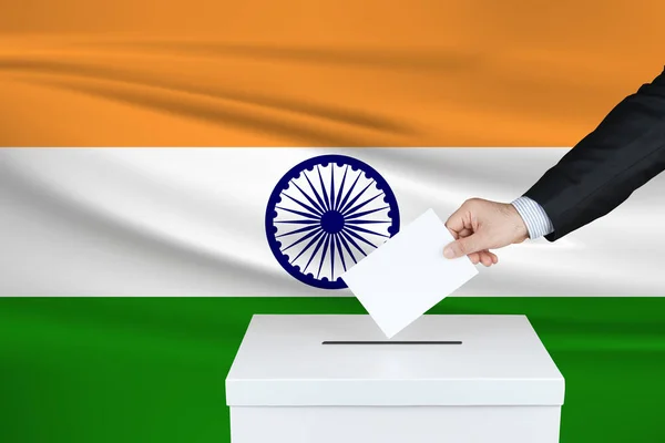 Election in India. The hand of man putting his vote in the ballot box. Waved India flag on background.