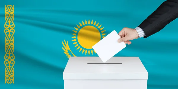 Election in Kazakhstan. The hand of man putting his vote in the ballot box. Waved Kazakhstan flag on background.