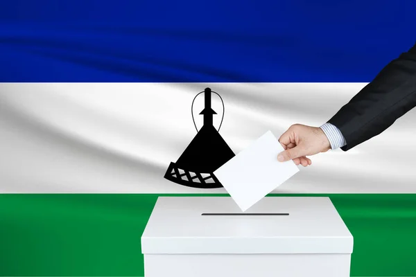 莱索托的选举 把他的选票放进投票箱的人的手 背风飘扬的莱索托国旗 — 图库照片