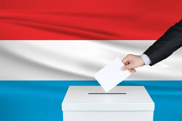 卢森堡的选举 把他的选票放进投票箱的人的手 背景是飘扬的卢森堡国旗 — 图库照片