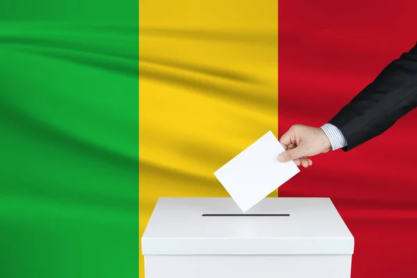 马里的选举 把他的选票放进投票箱的人的手 背景上飘扬的马里国旗 — 图库照片