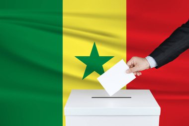 Senegal 'de seçim. Oylarını sandığa koyan adamın eli. Arka planda Senegal bayrağı sallandı.                               