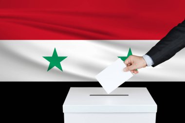 Suriye 'de seçim. Oylarını sandığa koyan adamın eli. Arka planda Suriye bayrağı sallandı.                               
