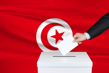 Tunus 'ta seçim. Oylarını sandığa koyan adamın eli. Arka planda dalgalı Tunus bayrağı.                               