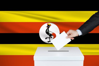 Uganda 'da seçim. Oylarını sandığa koyan adamın eli. Arka planda Uganda bayrağı sallandı.                               