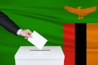 Zambiya 'da seçim. Oylarını sandığa koyan adamın eli. Arka planda Zambiya bayrağı sallandı.                               