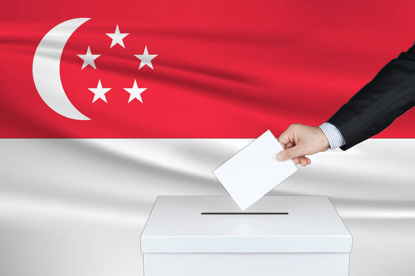 Выборы в Сингапуре. Рука человека, положившего свой голос в урну для голосования. Размахивал флагом Сингапура на заднем плане
.                               