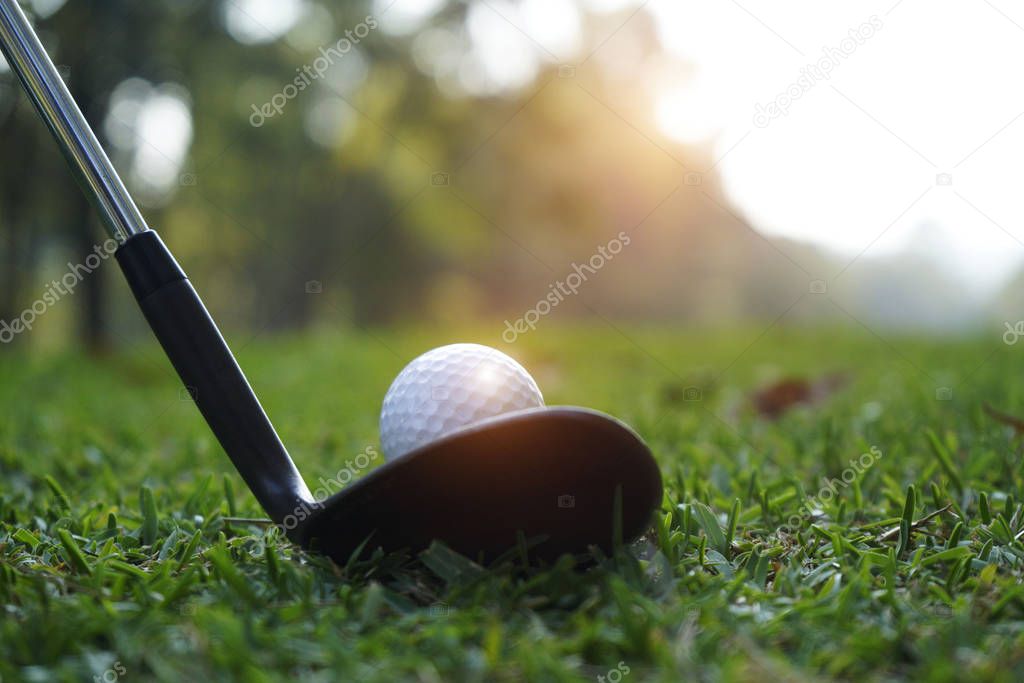 Blurred golf club and golf ball close up in grass field with sun