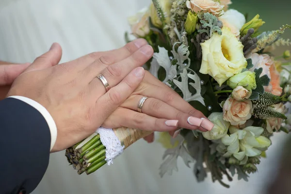 Mãos da noiva e noivo em anéis e um buquê de casamento — Fotografia de Stock