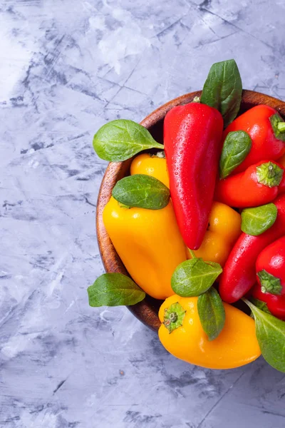 Red and yellow little bell peppers in a wooden plate on a gray background