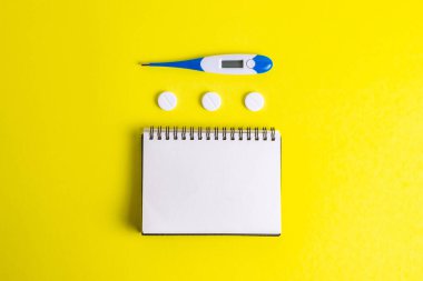 Sarı arka planda termometresi olan lastik eldivenli bir defter.