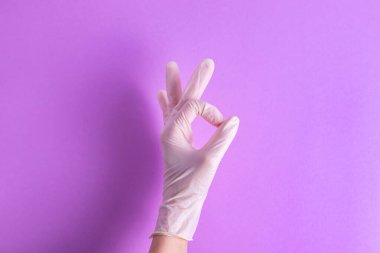 Tamam, mor arka planda lastik eldivenli bir el işareti.