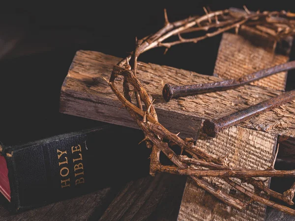 Closeup of wooden cross and crown of thorns with the holy bible in a dark rustic setting