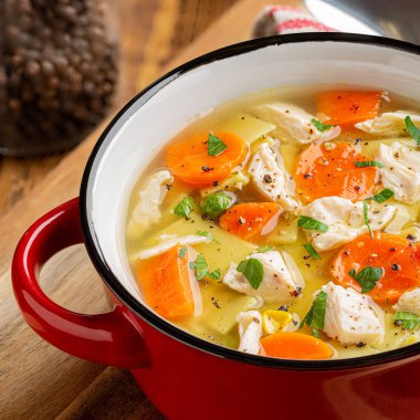 Bir kase tavuklu şehriye ve ahşap masada sebze çorbası.