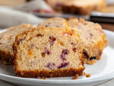Dilimlenmiş yaban mersinli, portakallı kekin beyaz tabakta yakın çekimi.