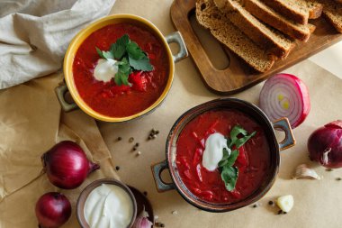 Bej bir zemin üzerinde borş çorbası. Kil tabakta sarımsak, soğan, biber, ekşi krema ve ekmek.