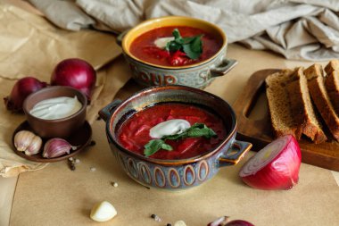 Bej bir zemin üzerinde borş çorbası. Kil tabakta sarımsak, soğan, biber, ekşi krema ve ekmek.