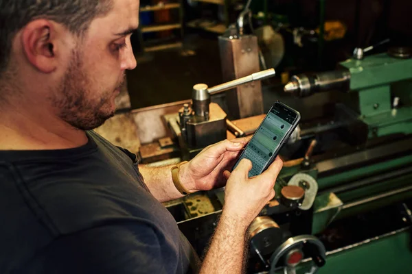 Fabrikadaki torna makinesini cep telefonu kullanarak kontrol eden makine mühendisi..