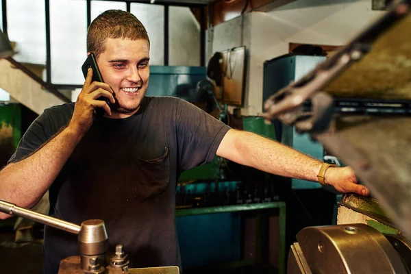 Fabrikadaki torna makinesini cep telefonu kullanarak kontrol eden makine mühendisi..