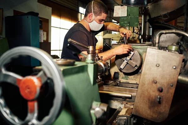 Mechanical Engineer Controlling Lathe Machine in Factory Protecting Himself with Coronavirus Mask