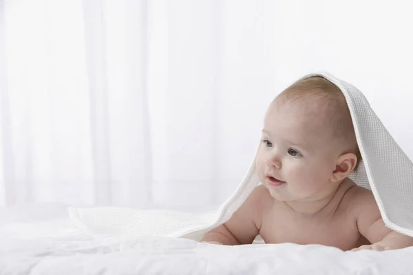 Baby som tittar upp från under täcket — Stockfoto