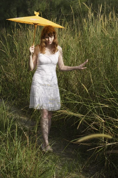 Vrouw wandelen in hoog gras met paraplu — Stockfoto