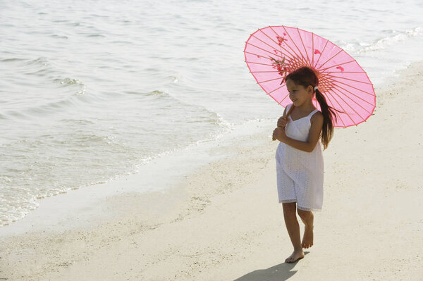 Little girl walking on beach under pink umbrella