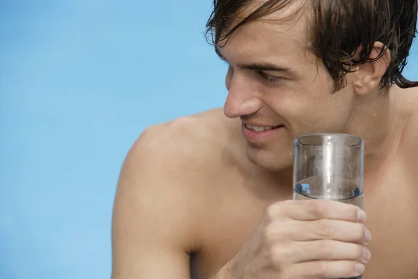 Mladý muž v bazénu se sklenicí vody — Stock fotografie