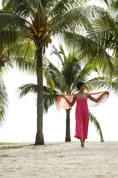 Mujer caminando en la playa bajo cocoteros vistiendo de rosa . — Foto de Stock