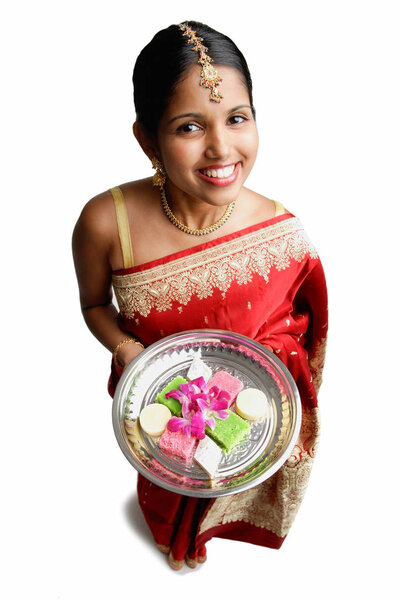 Woman in sari, holding plate of Indian cakes