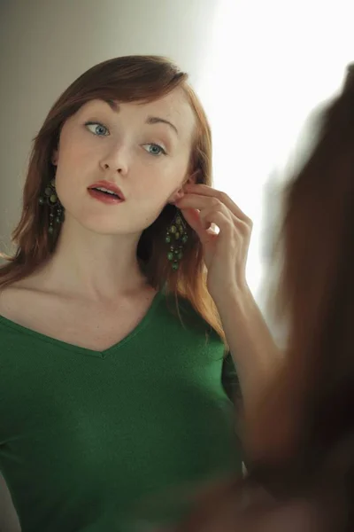 Vrouw probeert op oorbellen in spiegel — Stockfoto