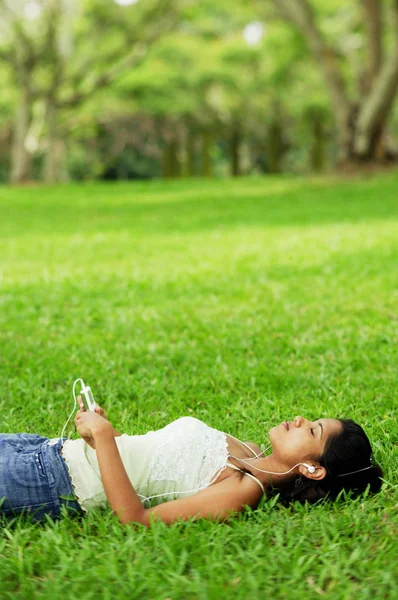 Woman listening to music lying on grass — Stock Photo, Image