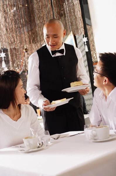 Pareja en restaurante, camarero de pie junto a su mesa — Foto de Stock