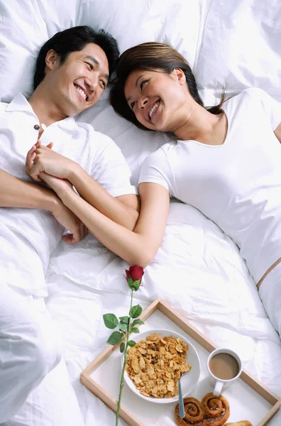 Пара лежащих на кровати, держащихся за руки — стоковое фото